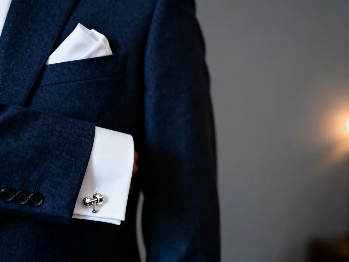 Granatowa marynarka z białą poszetką i eleganckimi spinkami do mankietów jako propozycja męskiej stylizacji na wesele.